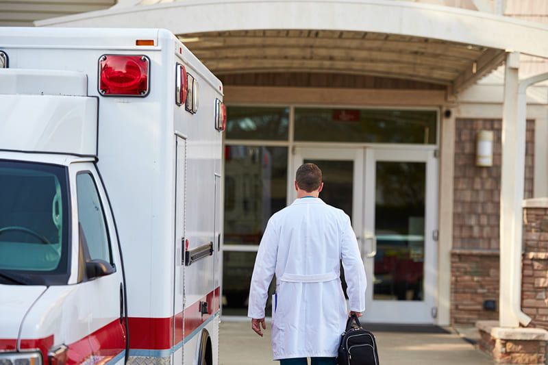 Вид сзади на врача, идущего от скорой машины к дому